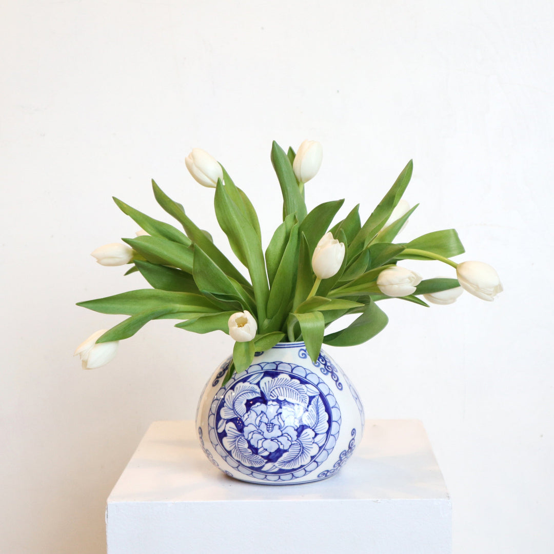 Elegant white tulips in a Delft blue vase on a white pedestal, perfect for home decor or gifting.