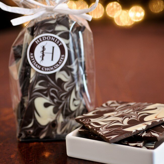 Hedonist Chocolate Bark | Espresso bark w/ a white swirl pattern. Bark displayed in a white dish with a clear back of bark in the background tied with a white bow.