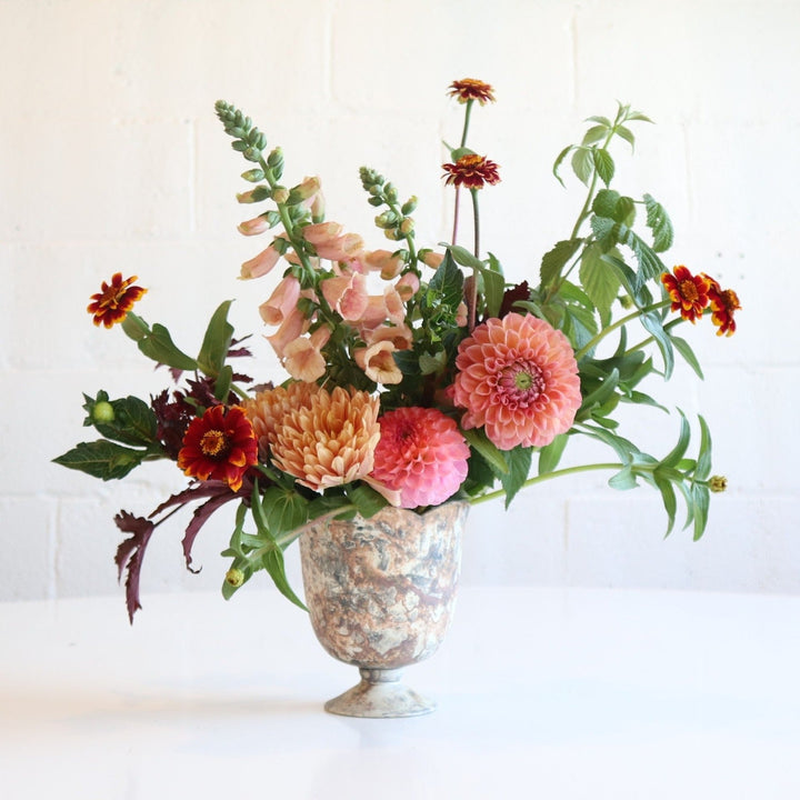 Serendipity | Fresh Floral Arrangement | Stacy K Floral | A summer arrangement with soft pinks, reds, and a hint of orange. Some of the flowers pictured are dahlias and snap dragons. Accented with greenery. The arrangement is in a marbled vase. Photo taken against a white background.