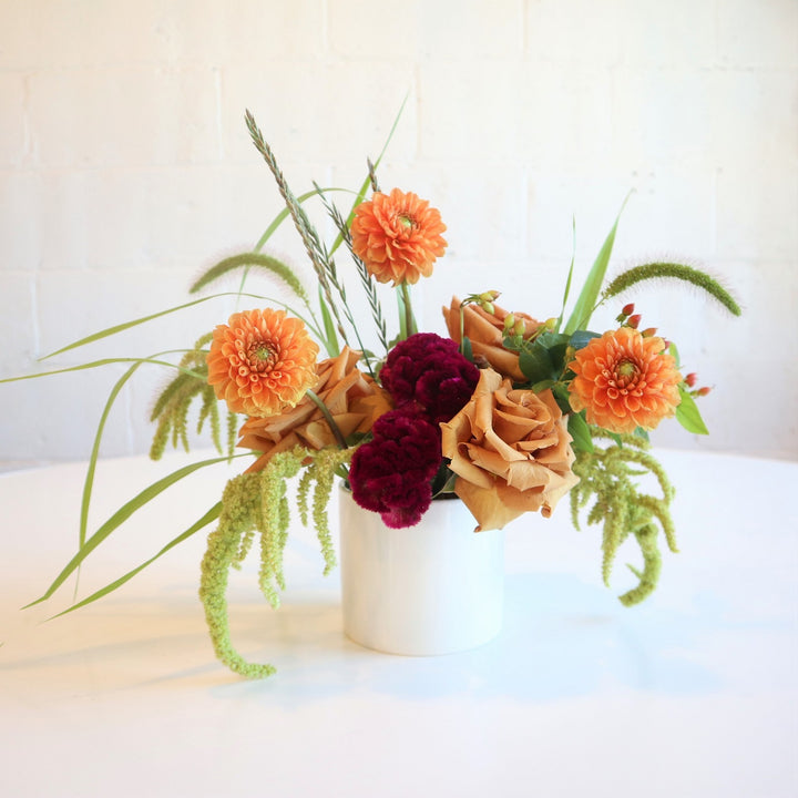 Golden | Stacy K Floral | Fresh Floral Arrangement | A fall colored arrangement with orange dahlia, red celosia, english toffee roses, and green ameranthus. Other accent greenery uses. Arrangement is in a classic white pot. Photo taken against an white background.
