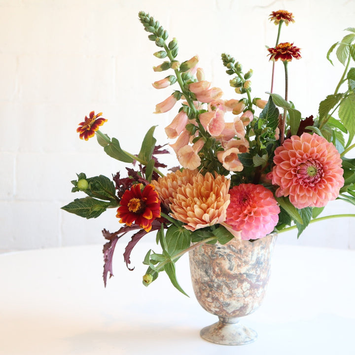 Serendipity | Fresh Floral Arrangement | Stacy K Floral | A soft pinks, red, and oranges arrangement featuring dahlias and snapdragons. Accented with a variety of greenery. In a marbled vase. Photo taken against a white background.
