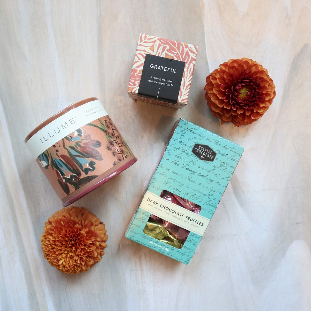Grateful Gift Box | An illume candle with a brown floral label, "Grateful" pop-open cards, and dark chocolate truffles by Seattle Chocolate. Dahlias placed around as decoration.
