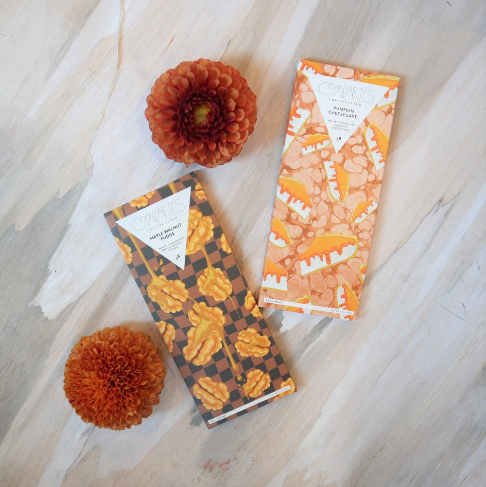 Fall Gift Box | Close up on the Compartes chocolate bars. Flavors shown "Maple Walnut Fudge" and "Pumpkin Cheesecake". Photo accented with orange dahlias.