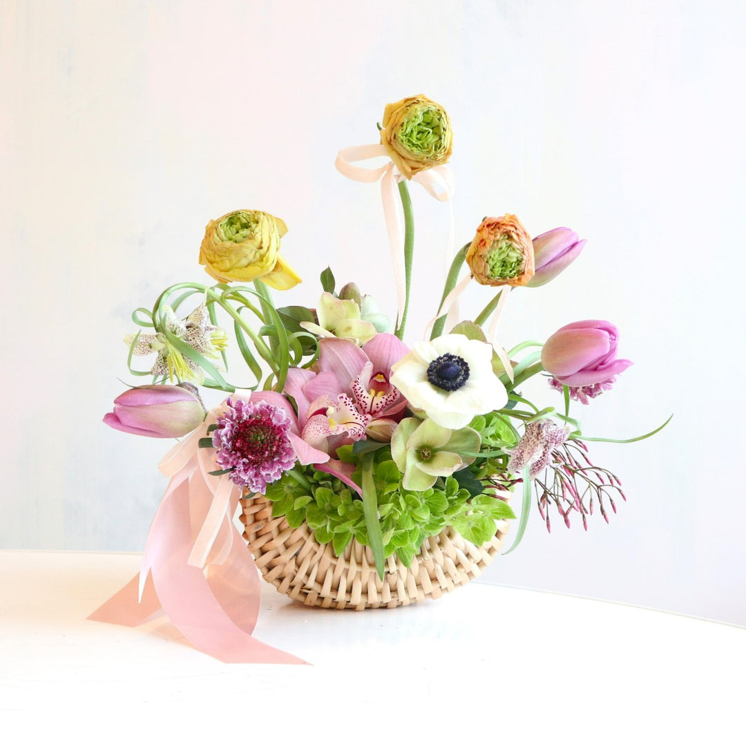 Petals & Charm Basket | A bright spring arrangement with whites, greens, pinks, and orange. Some flowers pictured are orchids, tulips, and hydrangea. Made in a woven basket.