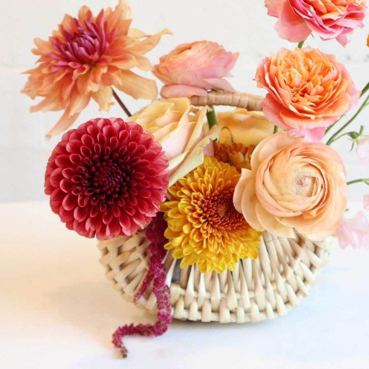 fall basket with orange dahlias, bronze mums, ranunculus, marigolds, light pink sweet pea, and peach roses close up. 