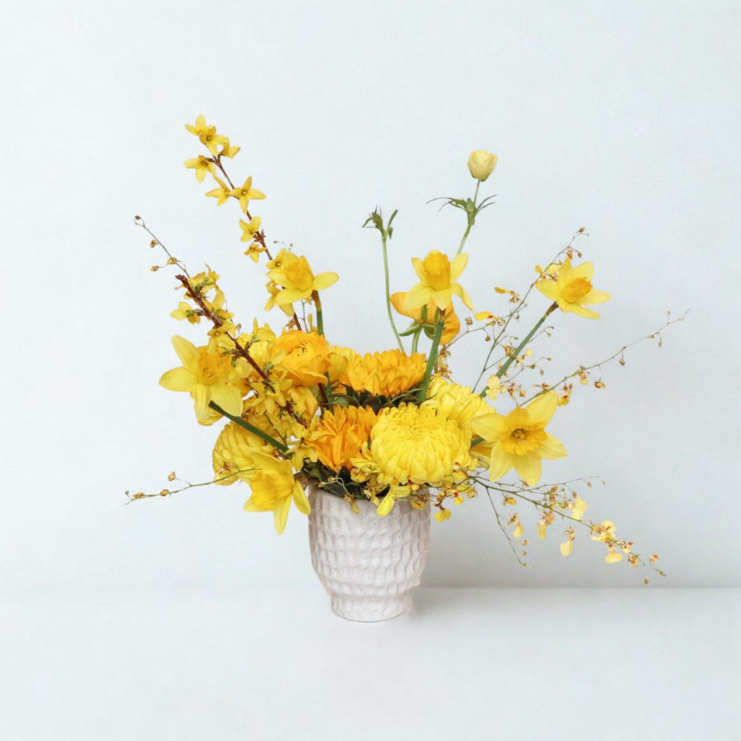 Stacy K Floral | Bright yellow spring flower arrangement with daffodils, ranunculus, mums, and forsythia in a white ceramic vase by Rochester NY florist
