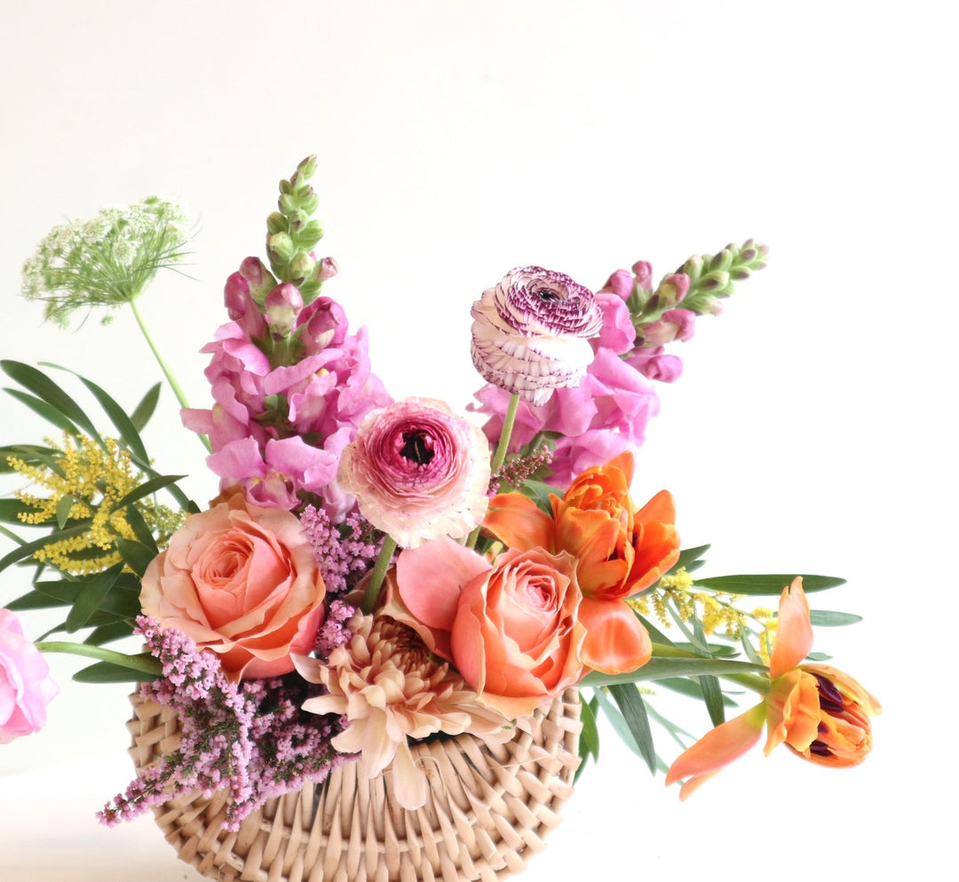 Basket of spring flowers with ranunculus, snapdragons, tulips, queen annes lace, heather, acacia.