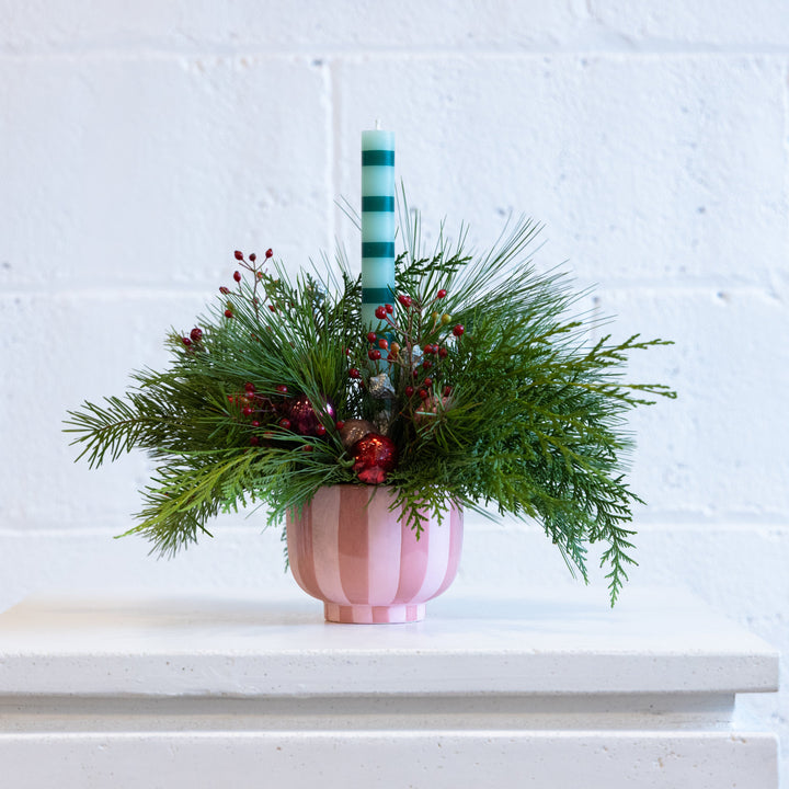 Decorative arrangement with a striped candle in a pink vase on a white surface.