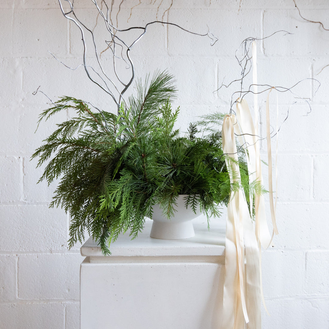 Greenery arrangement in a white vase against a white brick wall