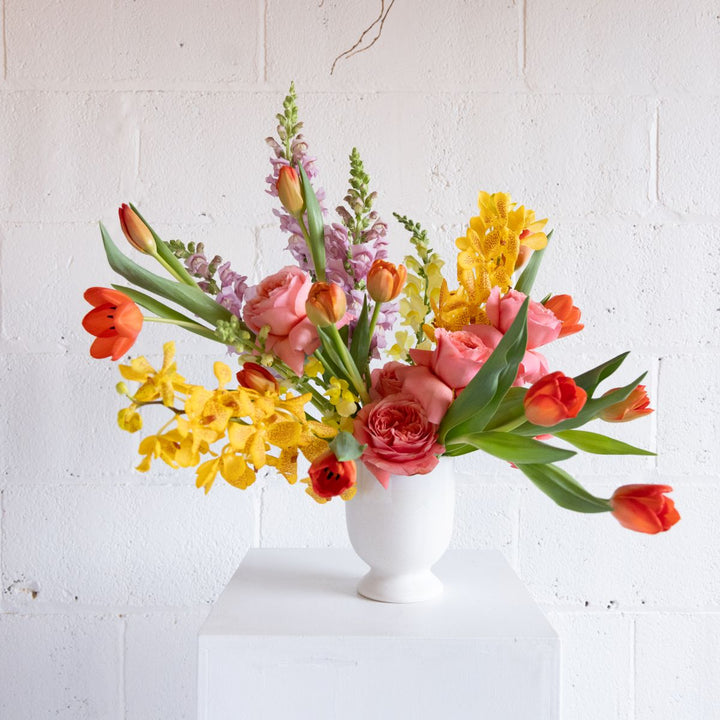 a bright spring arrangement with tulips, roses, orchids, and snap dragons. 