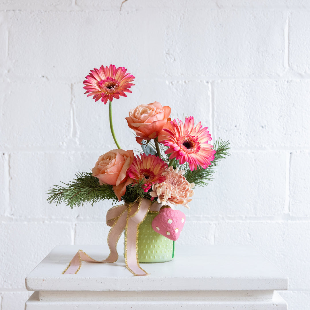 Floral arrangement with pink and peach flowers in a textured green vase on a white surface.