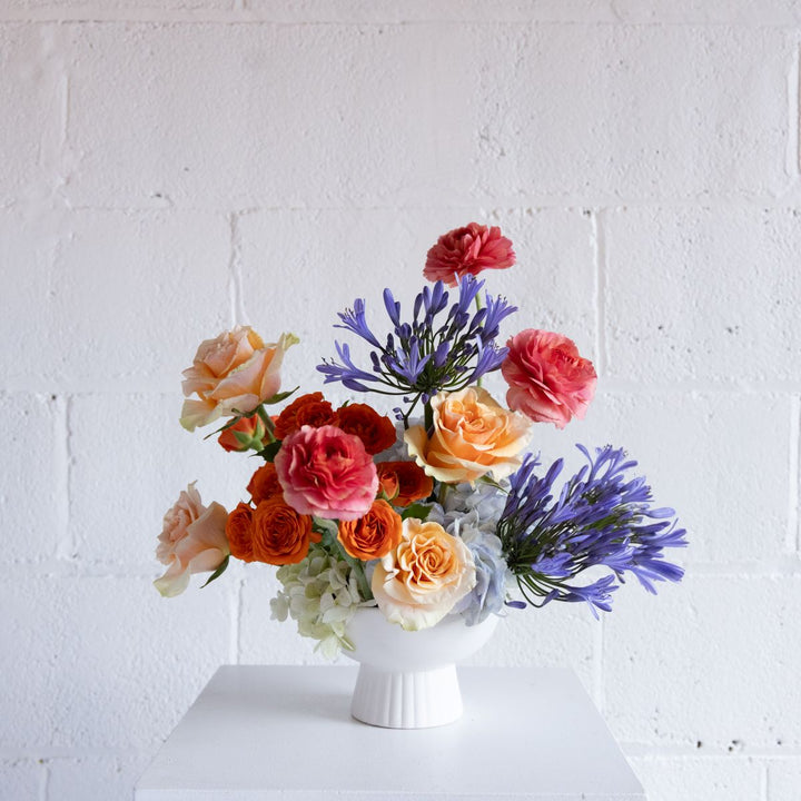 Colorful flower arrangement in a white vase against a white brick wall.