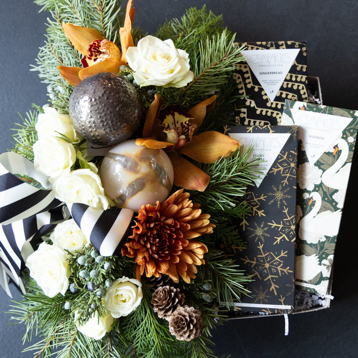 Decorative floral arrangement with pinecones and flowers, accompanied by chocolate bars  on a dark background.