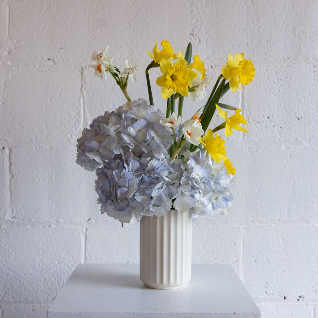Vase with yellow and white flowers against a white brick wall