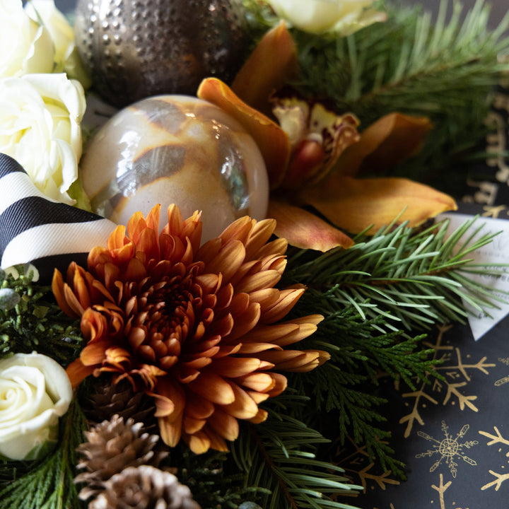 Decorative arrangement with flowers, pine cones, and a ribbon on a dark background