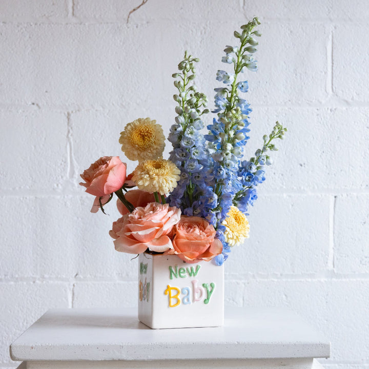 Floral arrangement in a 'New Baby' box against a white brick wall.