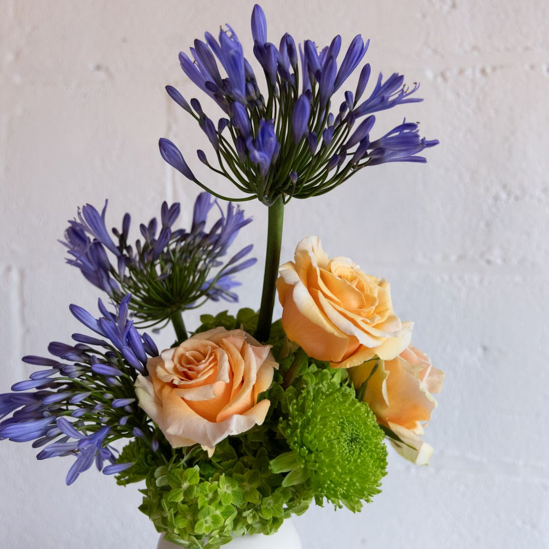Floral arrangement with purple flowers, orange roses, and green foliage on a white background