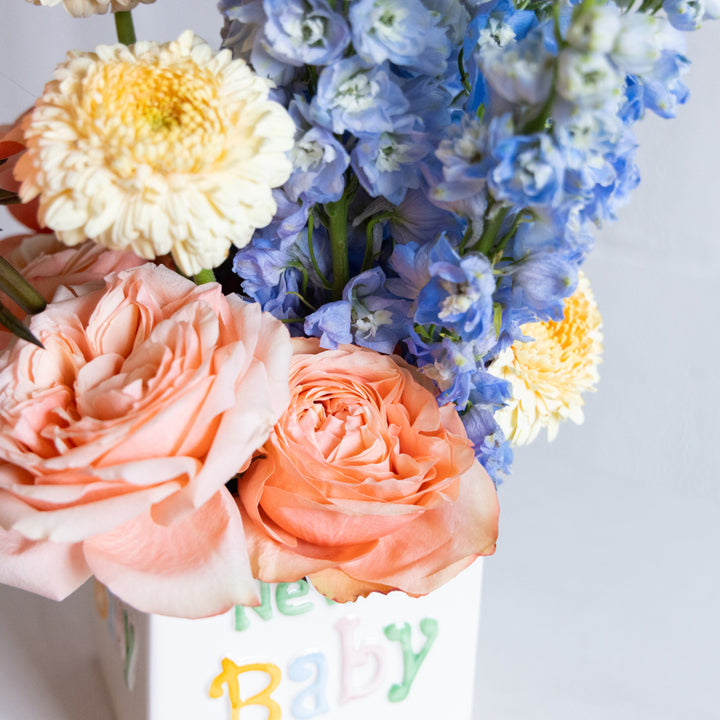 Bouquet of flowers with a 'Happy Baby' card on a light background