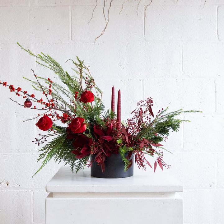 Decorative floral arrangement with red flowers and greenery on a white surface.