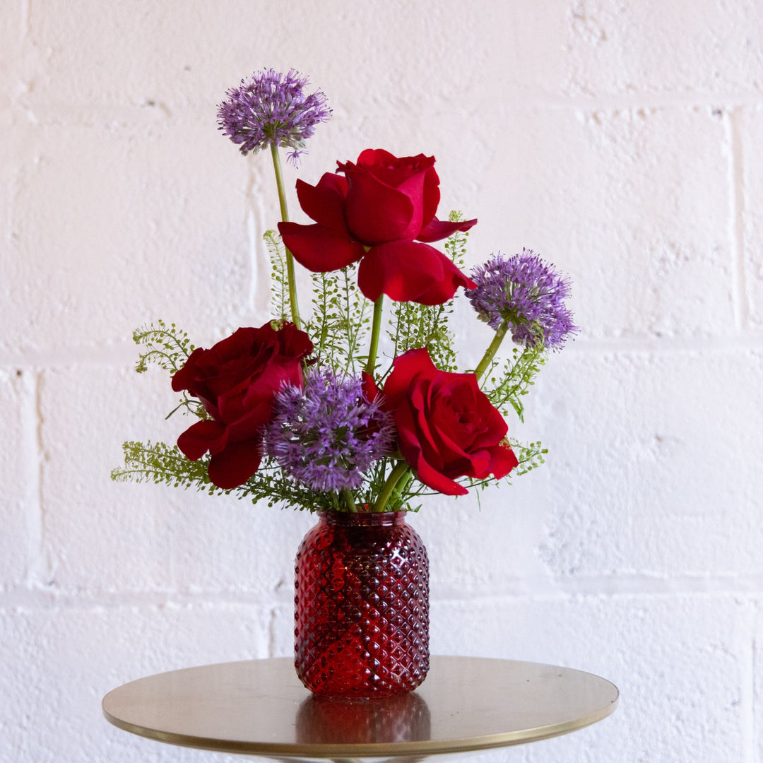 Bouquet of red roses and purple flowers in a textured red vase