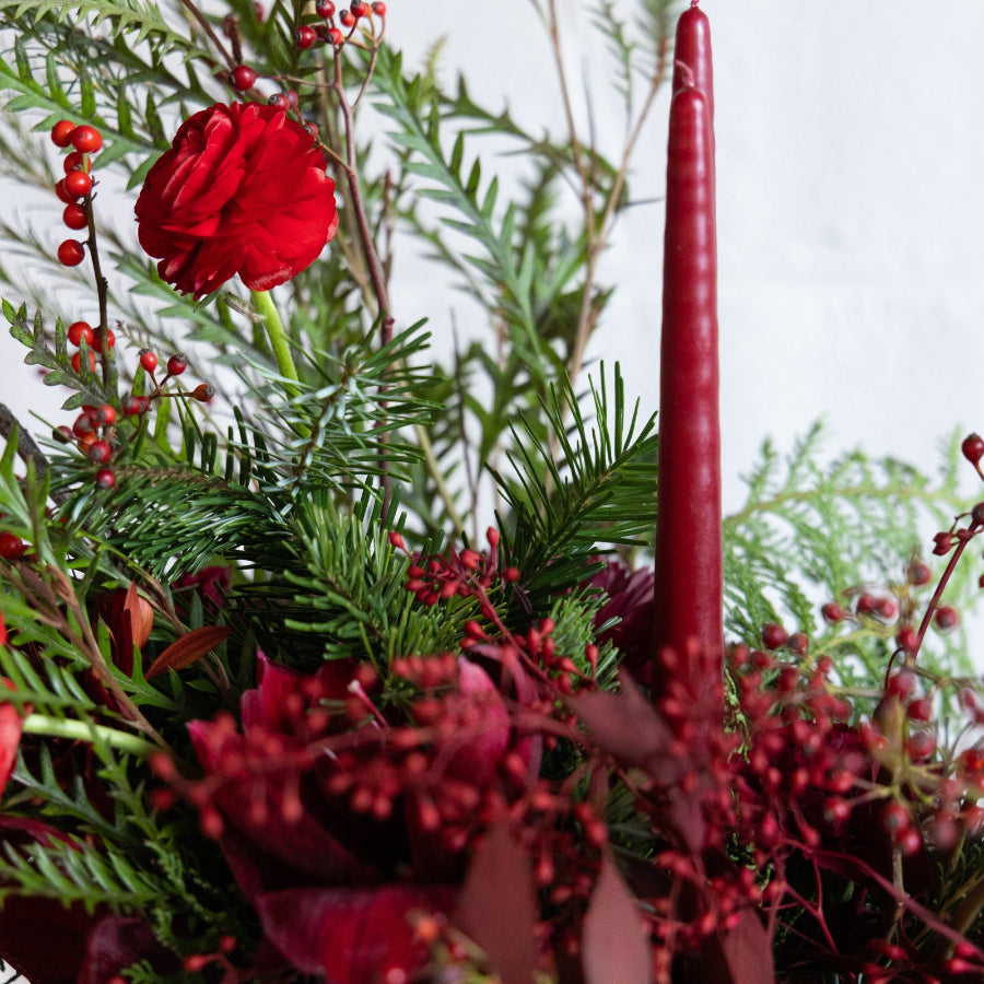 Decorative arrangement with red flowers, berries, and a tall red candle.