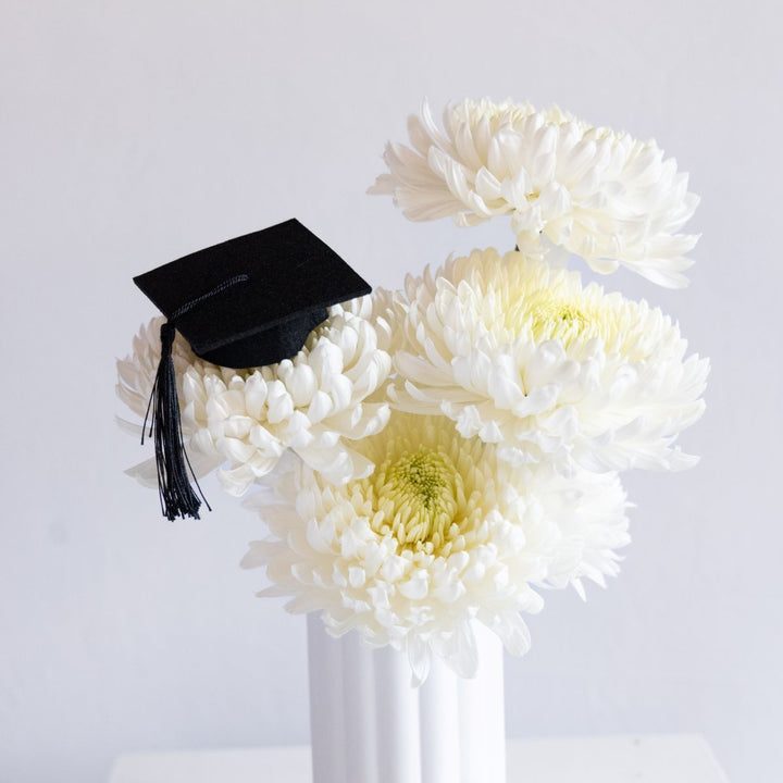 Graduation cap on a bouquet of white flowers against a light gray background