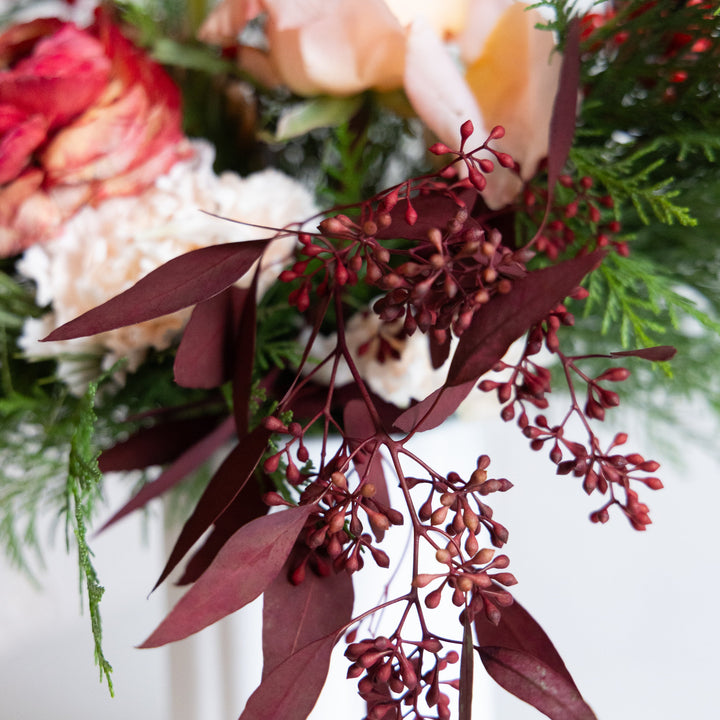 Close-up of a floral arrangement with red leaves and greenery on a white background