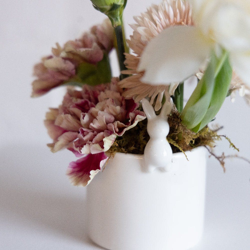 Small white vase with pink and white flowers and a small white rabbit figurine on a light background