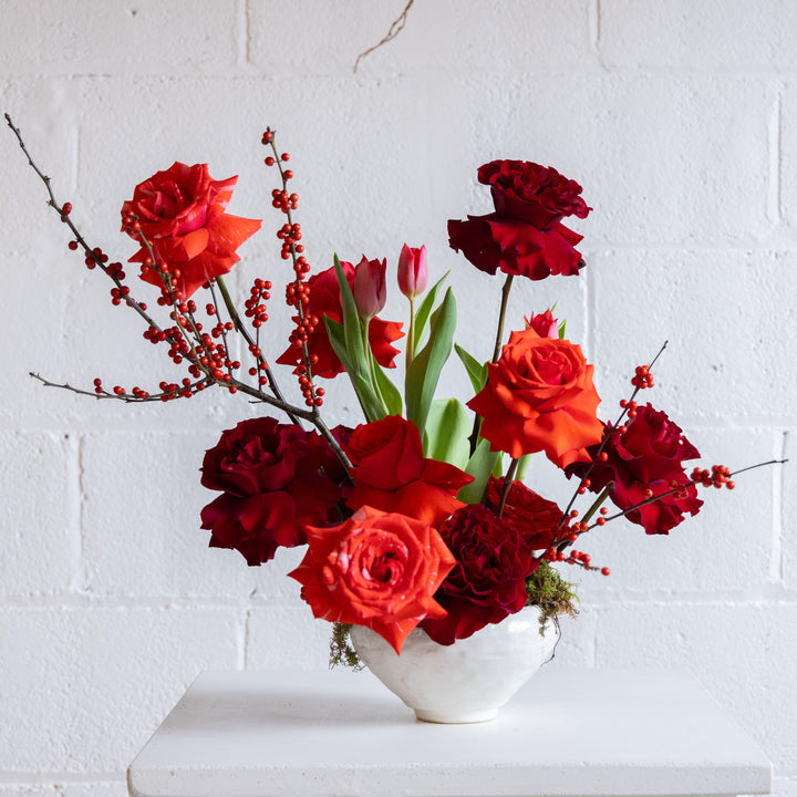 Bouquet of red and orange flowers in a white vase against a white brick wall.