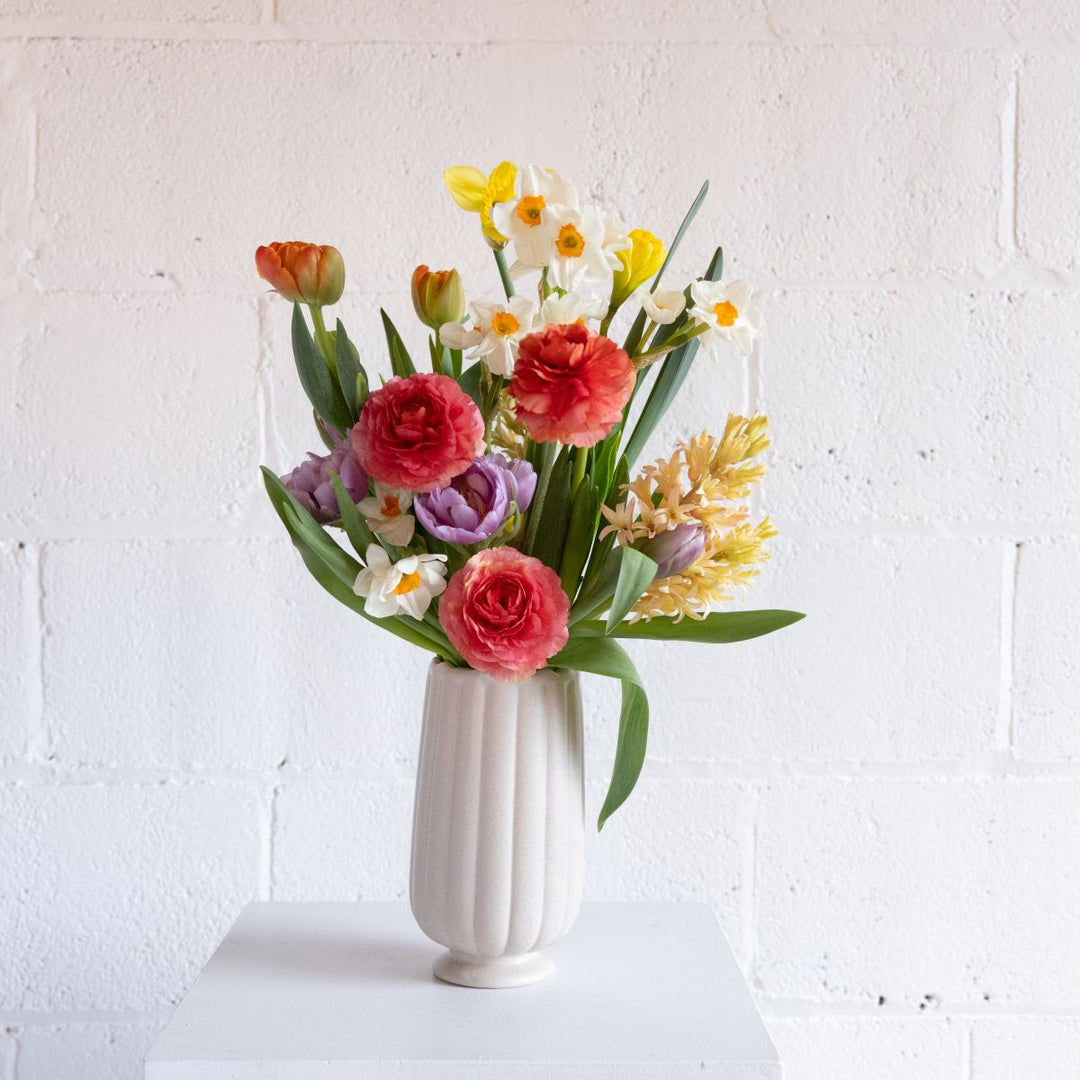 Bouquet of colorful flowers in a white vase against a white brick wall.