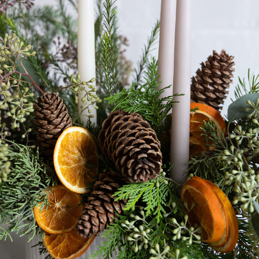 Decorative arrangement with candles, pinecones, and oranges in a festive setting.