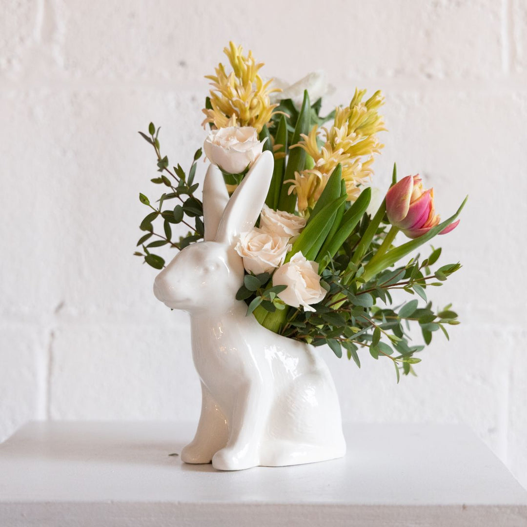 Floral arrangement in a white ceramic bunny vase on a light background