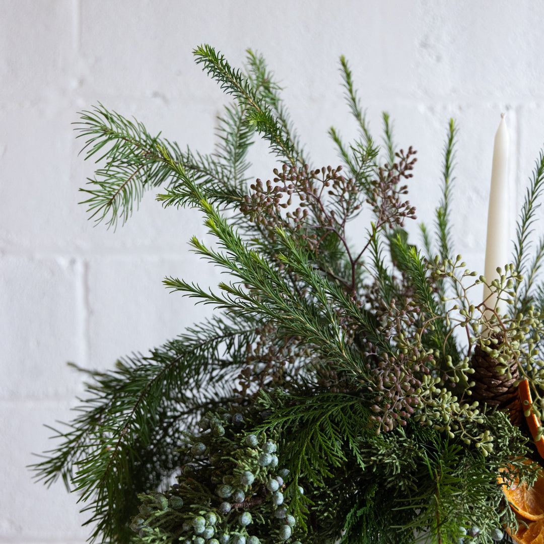 Decorative wreath with greenery and berries against a white brick wall