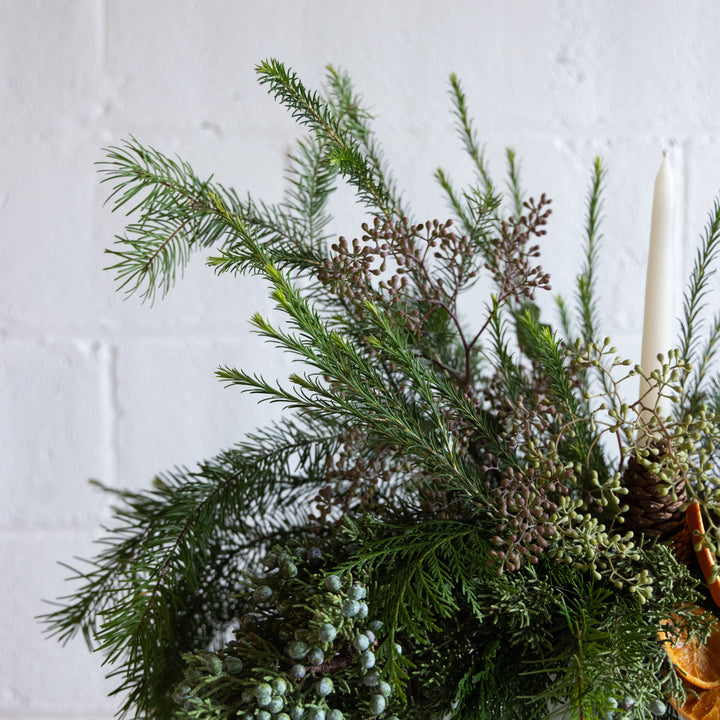 Decorative wreath with greenery and berries against a white brick wall