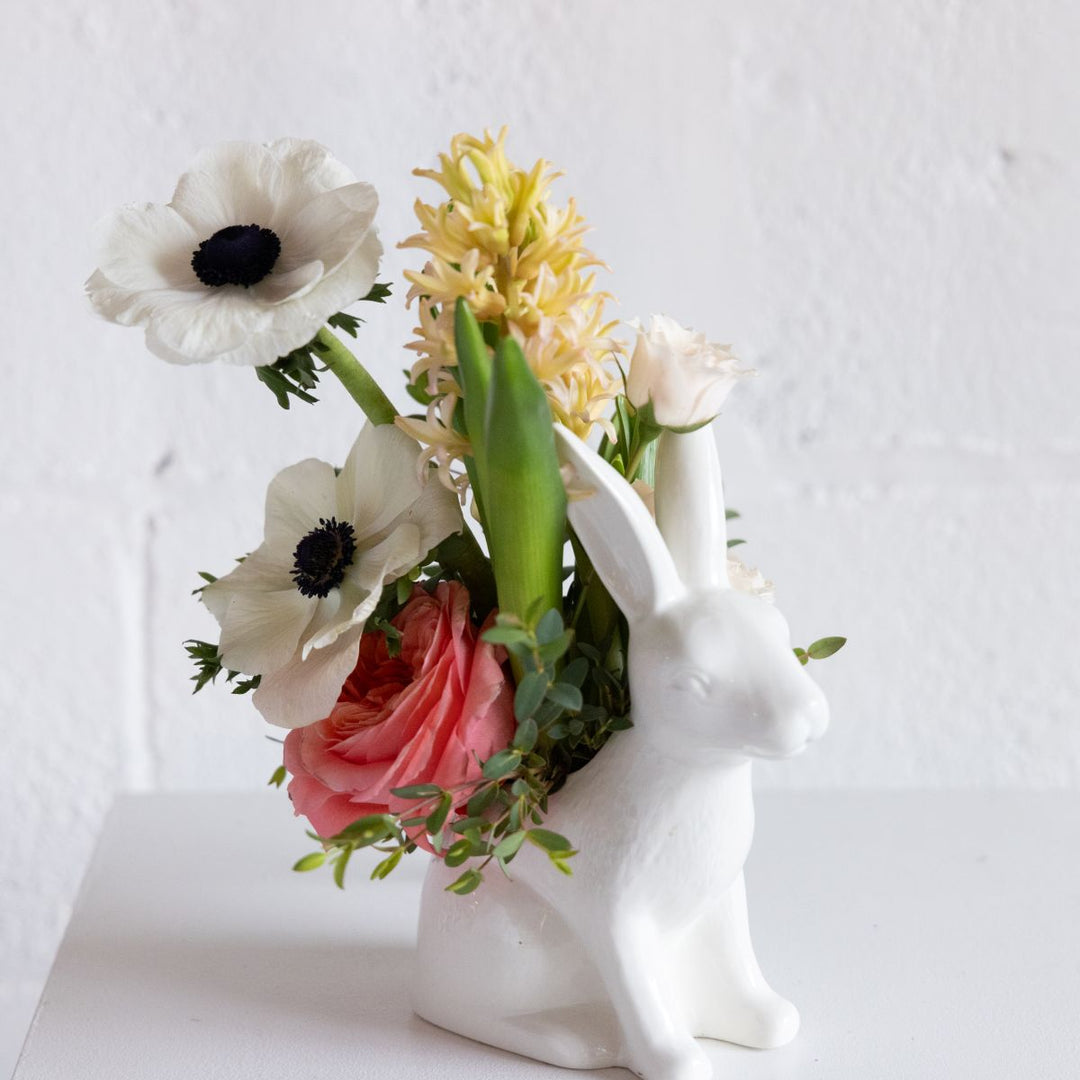 Floral arrangement in a white ceramic bunny vase on a light background