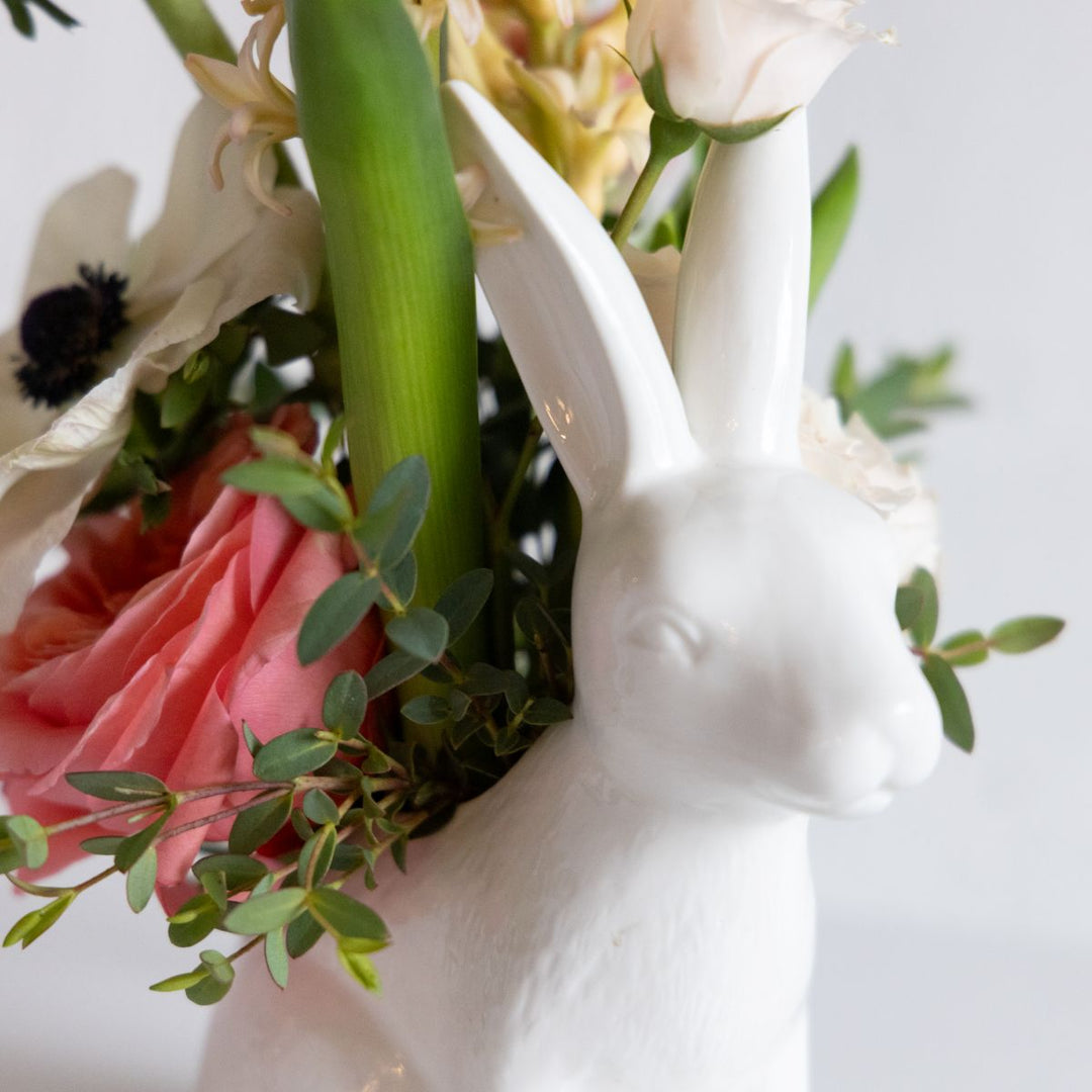 Floral arrangement in a white ceramic bunny vase on a light background