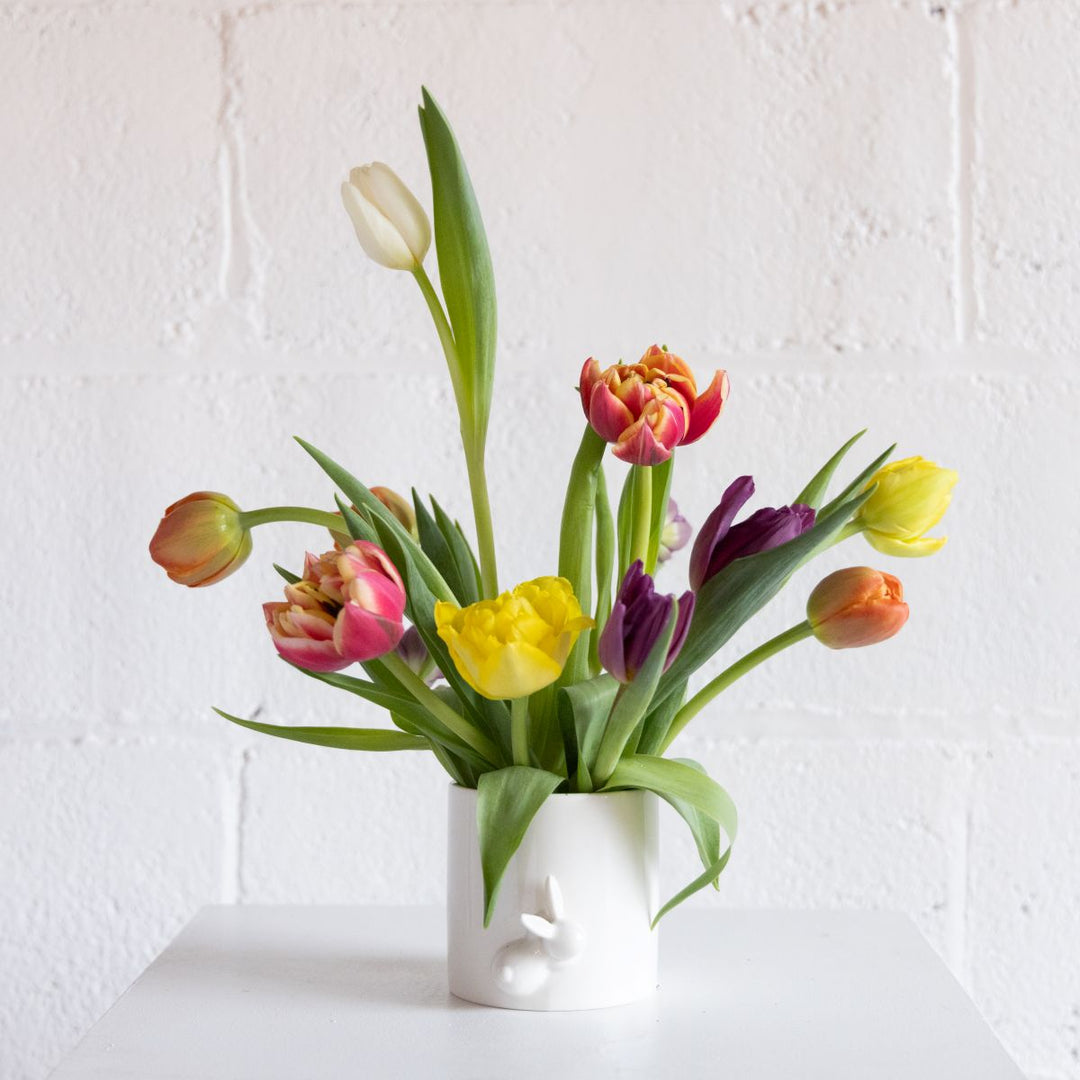 Floral arrangement of colorful tulip in a white ceramic vase with a bunny on it with a white background