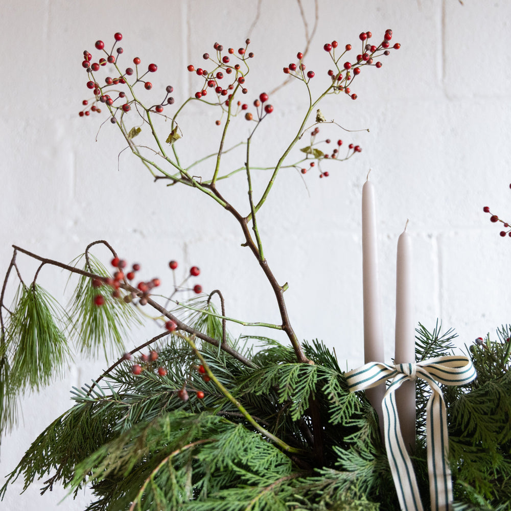 Decorative arrangement with greenery, red berries, and candles on a white background