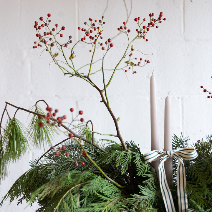 Decorative arrangement with greenery, red berries, and candles on a white background