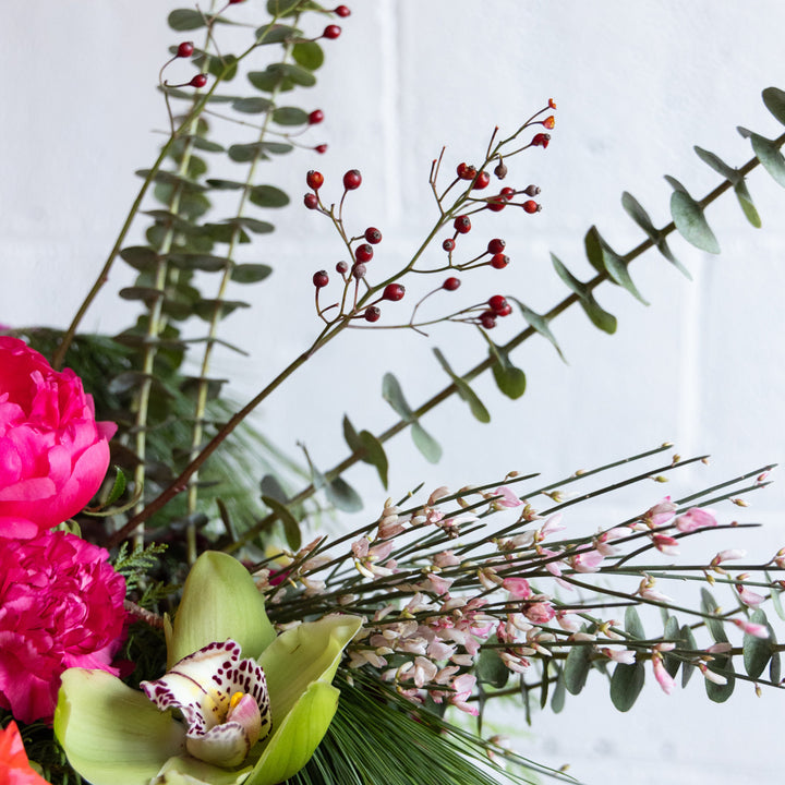 Bouquet of flowers with pink roses, green orchids, and red berries on a light background