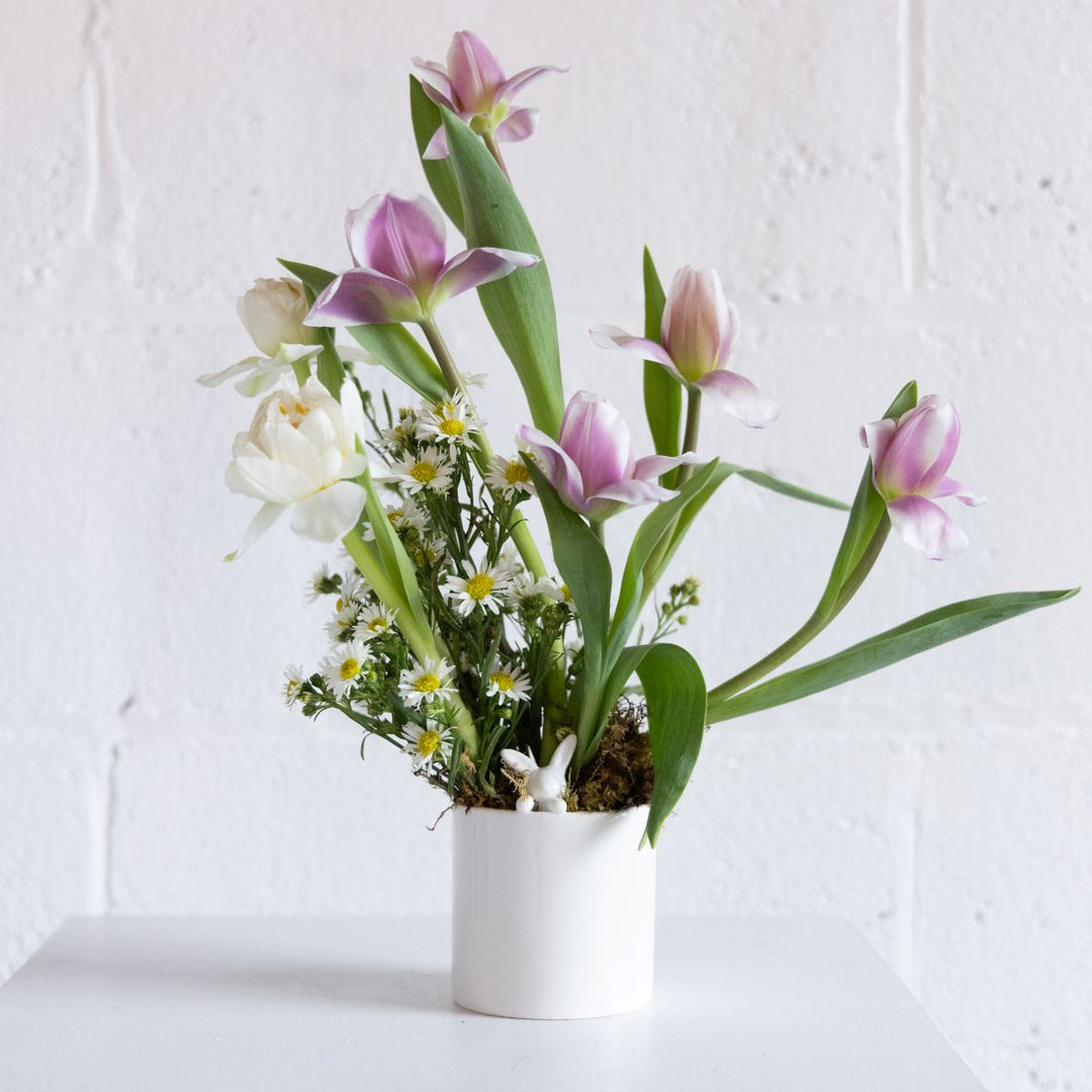 Floral arrangement with pink and white tulips in a white pot on a light background