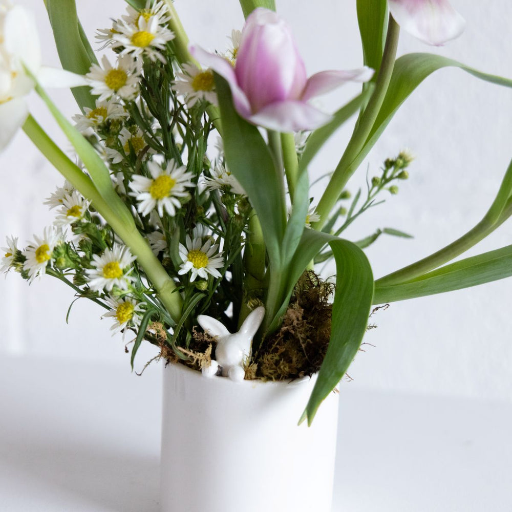 Floral arrangement with pink tulips and white daisies in a white vase on a light background