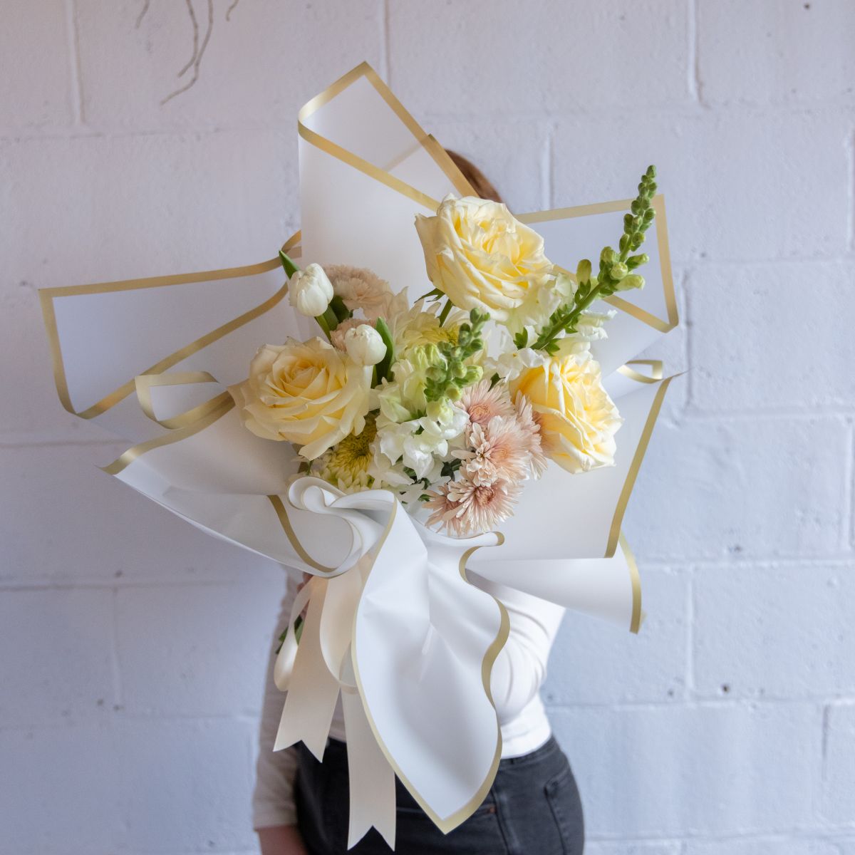 Bouquet of flowers with a decorative bow against a white brick wall.