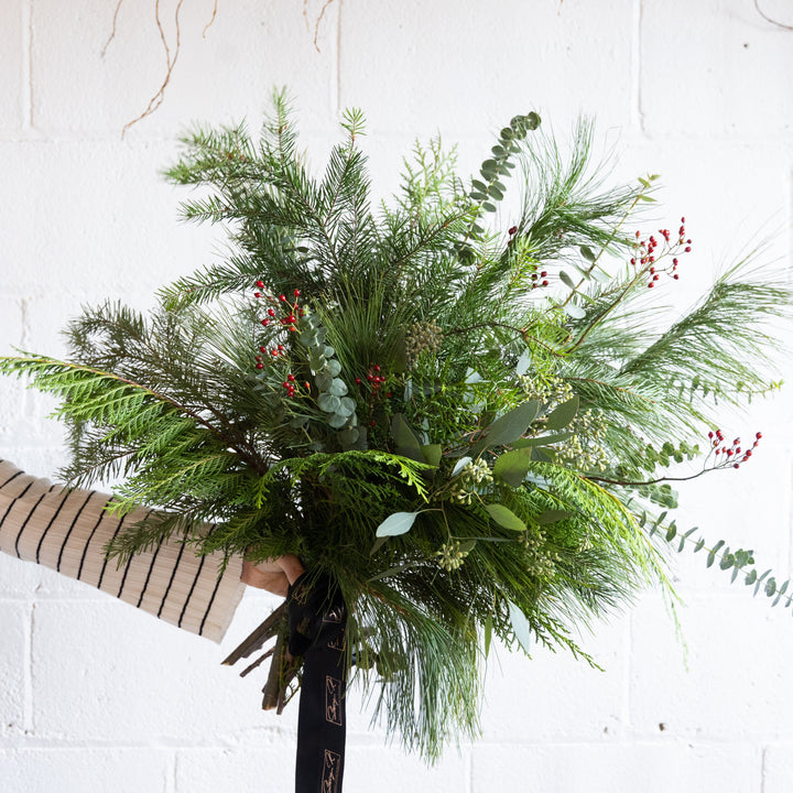 Bouquet of greenery held by a person against a white brick wall