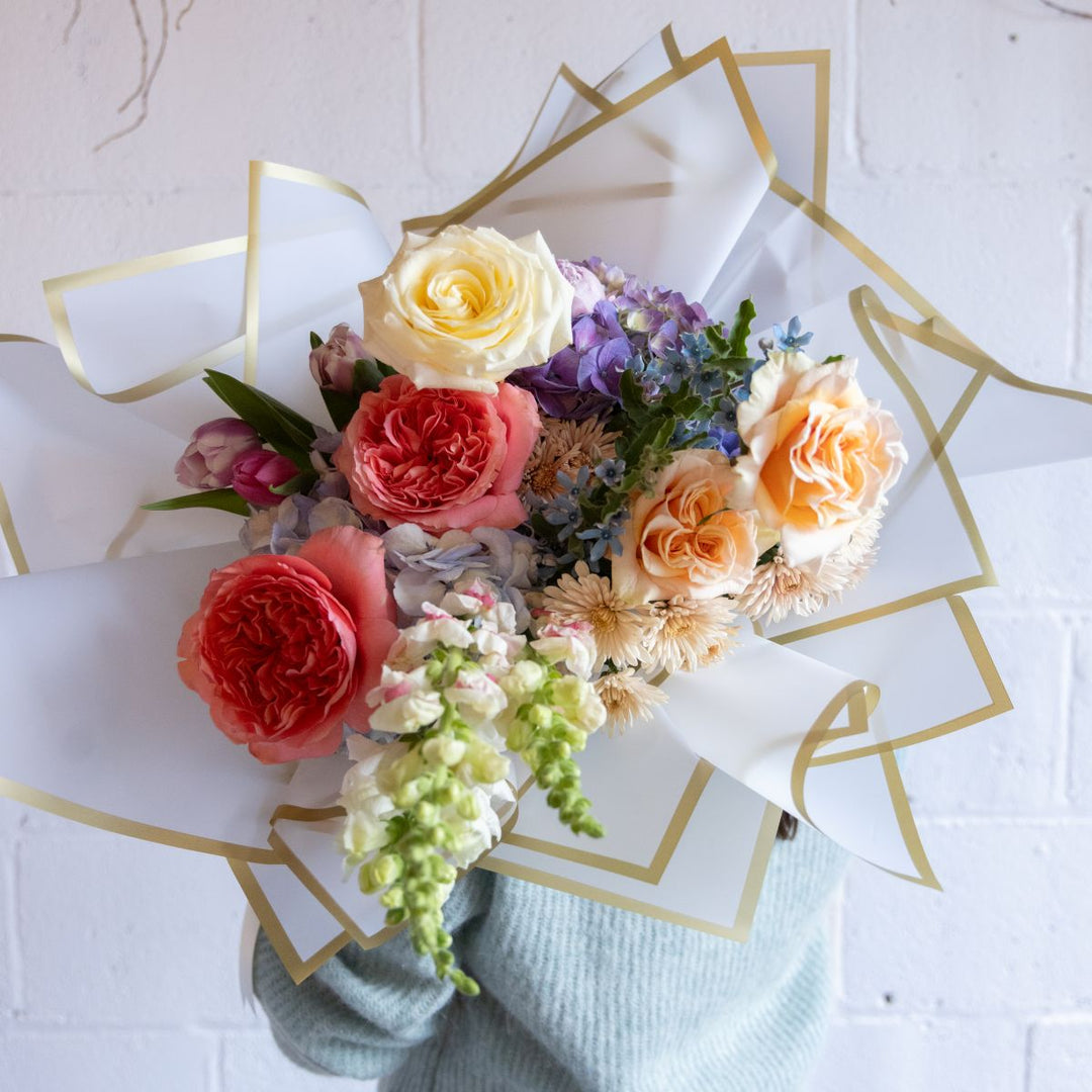 Bouquet of colorful flowers wrapped in white paper with gold accents on a white background