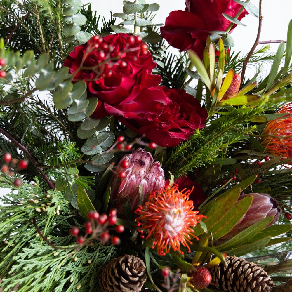 Close-up of a floral arrangement with red roses, greenery, and proteas.