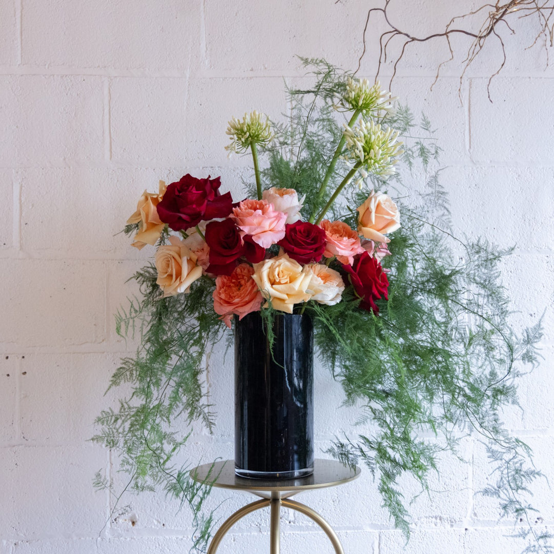 Floral arrangement with red, pink, and yellow flowers in a black vase on a white background
