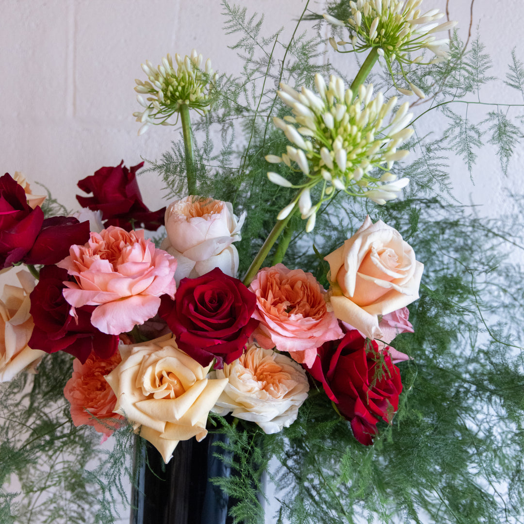 Bouquet of red, pink, and white roses with greenery on a light background