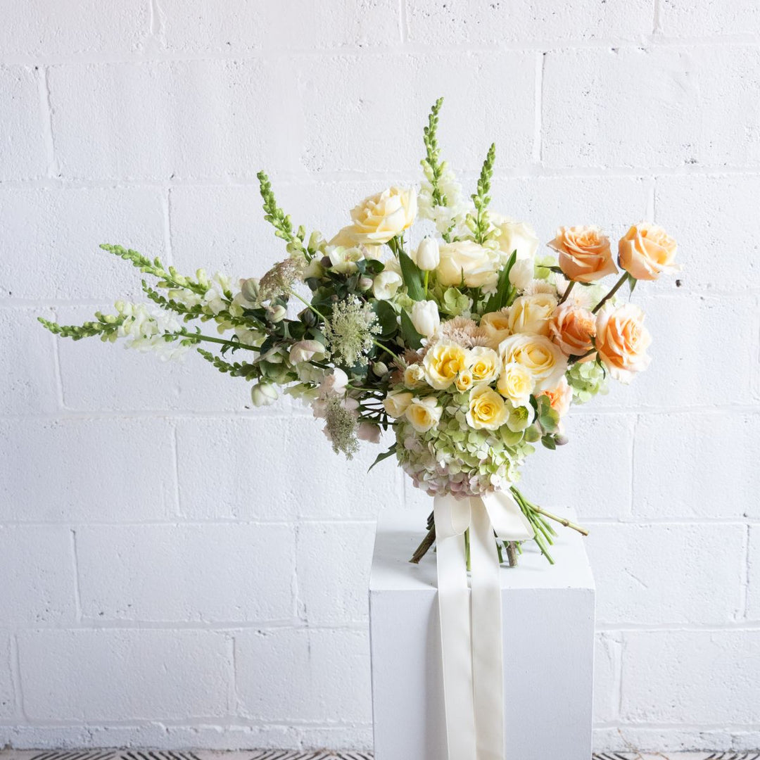 Bouquet of flowers on a white pedestal against a white brick wall
