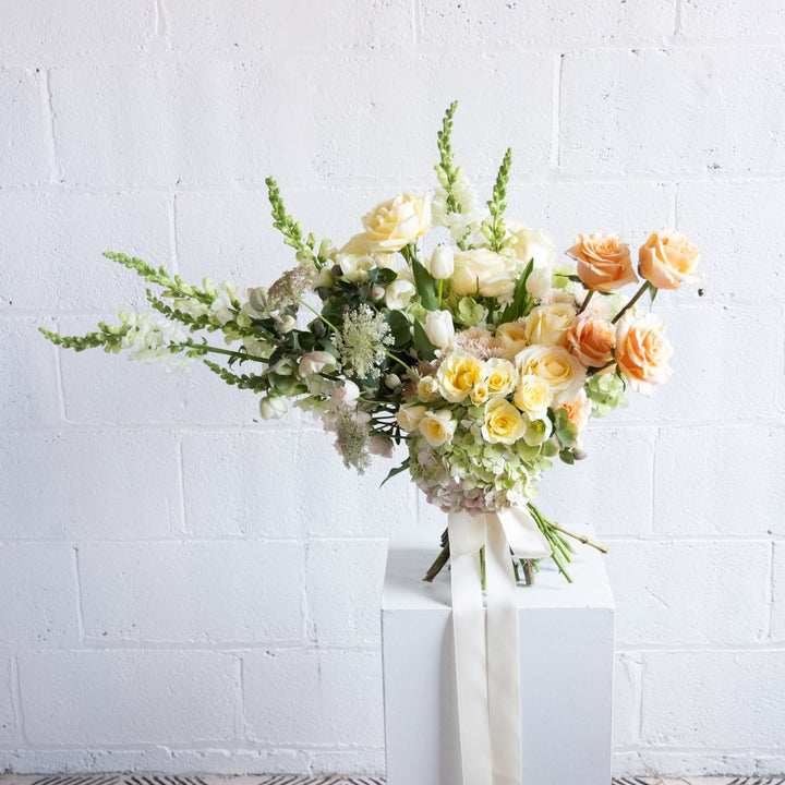 Bouquet of flowers on a white pedestal against a white brick wall